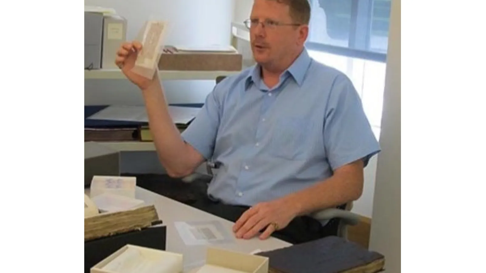 A man sits at a desk with a blue shirt on