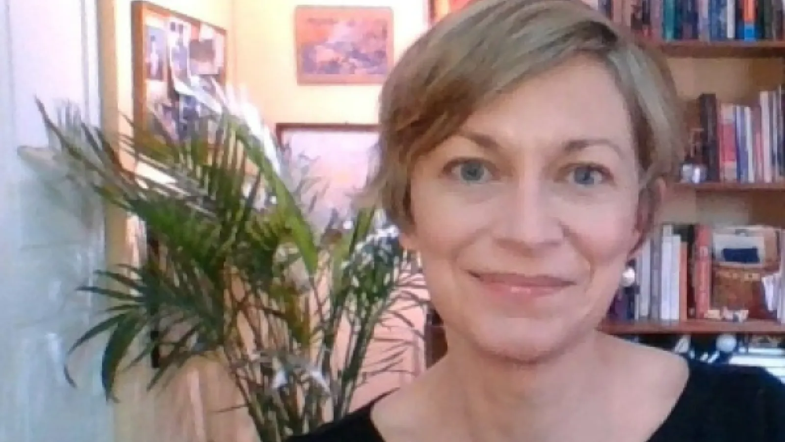 A front facing portrait of a white woman with short blonde hair in front of a bookcase