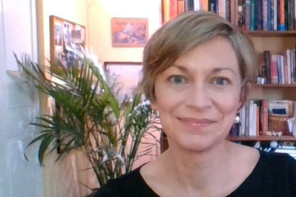 A front facing portrait of a white woman with short blonde hair in front of a bookcase